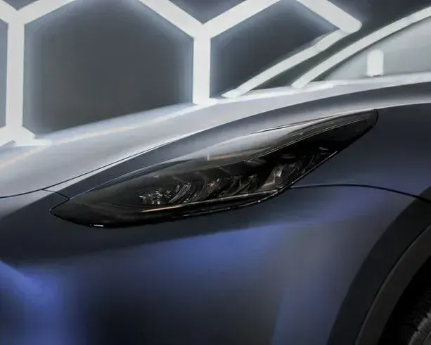 Dark blue car, close-up of headlight and front hood. Lit with honeycomb-shaped lights in the background.