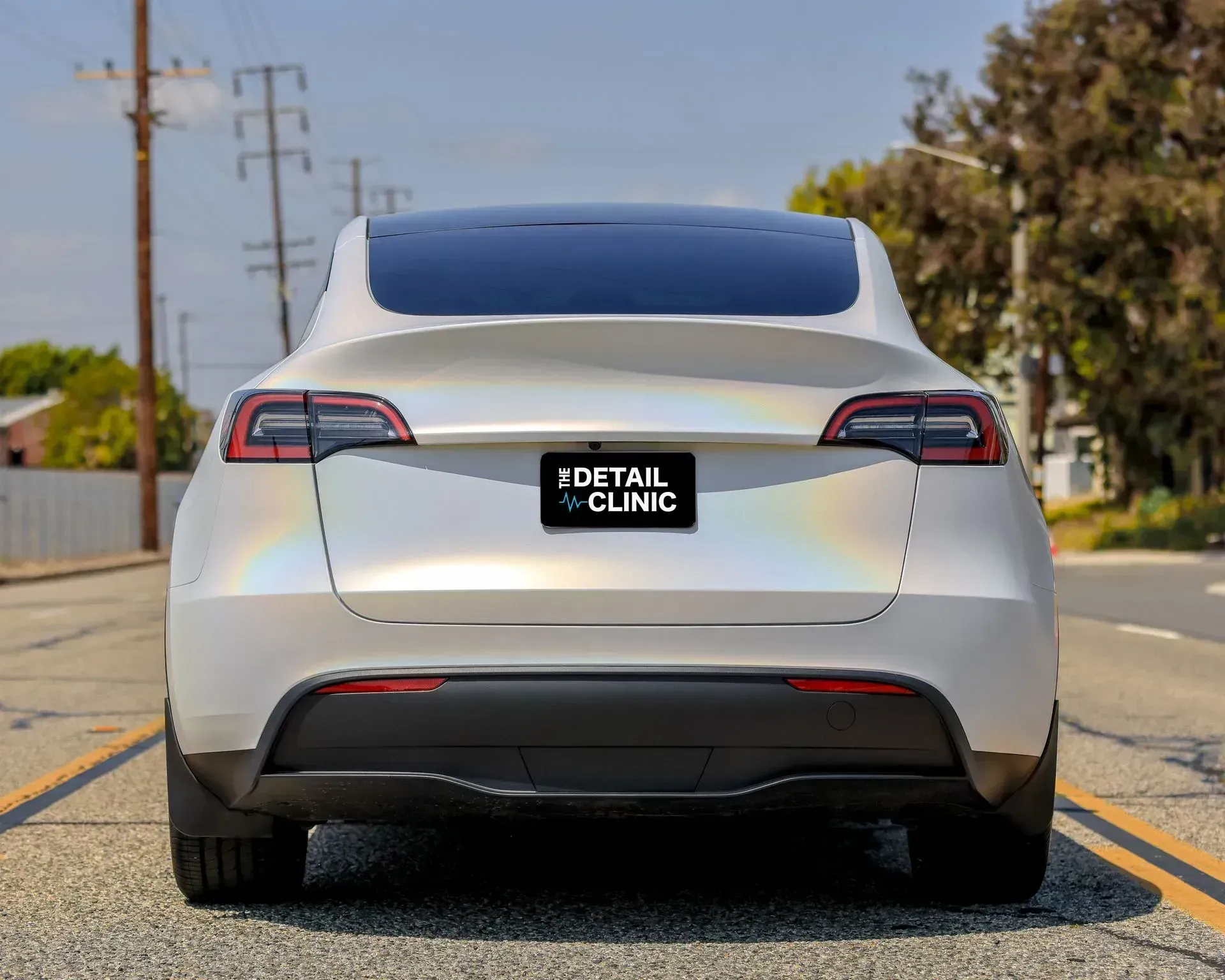 Rear view of a white Tesla SUV with iridescent finish, parked on a road.