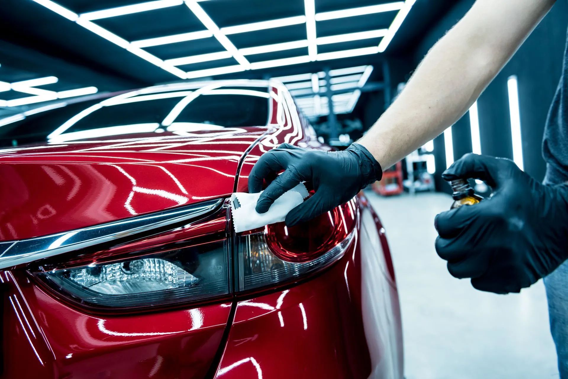 Person applying ceramic coating to a red car's tail light, wearing black gloves.