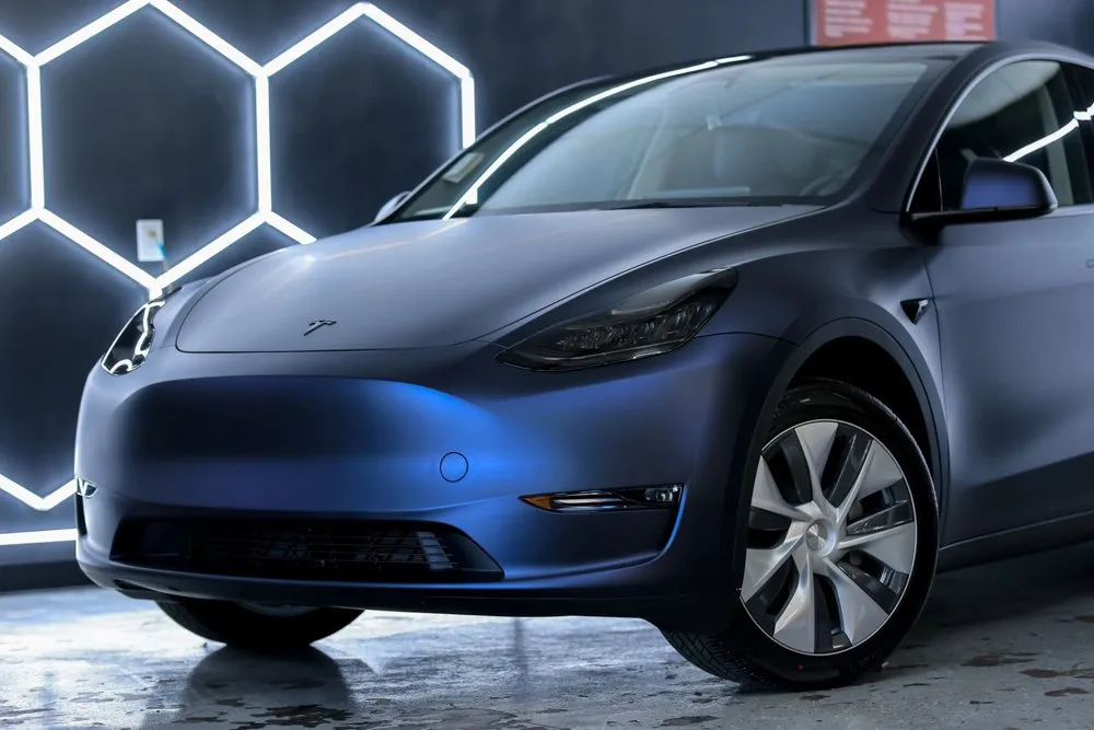 Blue Tesla Model Y electric SUV parked in a car wash bay with hexagon lights.