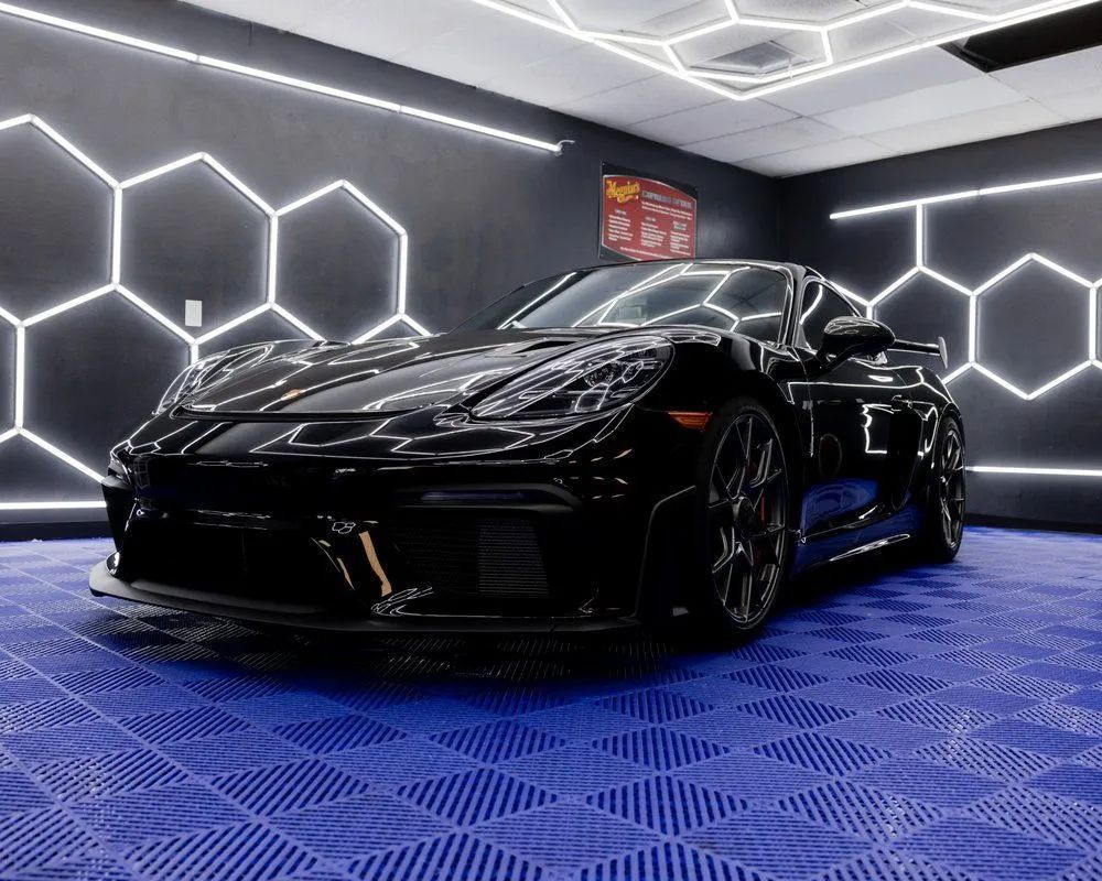 Black Porsche sports car in a garage with blue tiled floor and hexagon-shaped neon lights on the walls.