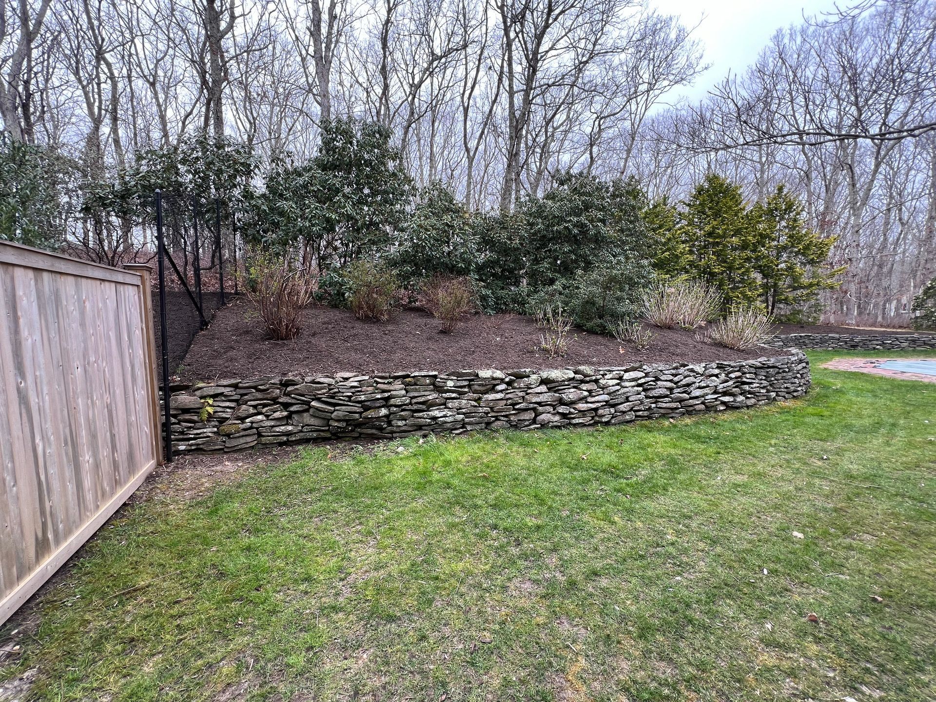 A backyard with a stone wall and a wooden fence.
