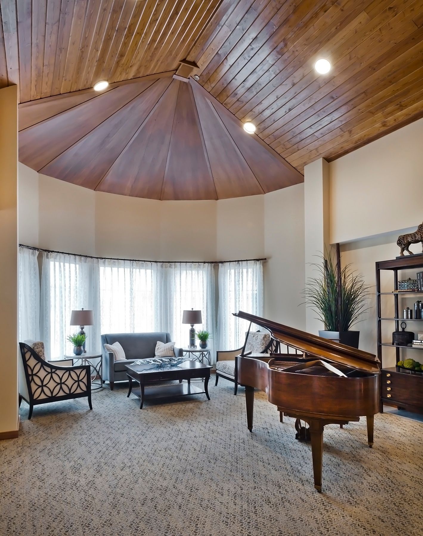 Grand piano in a bright living room with vaulted wood ceiling, seating area, and large windows