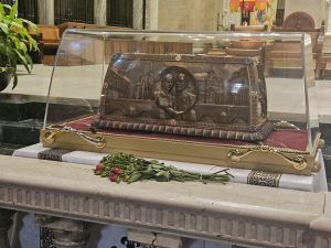A reliquary containing the remains of Saints Louis and Zélie Martin in a glass display case with flowers on an altar.