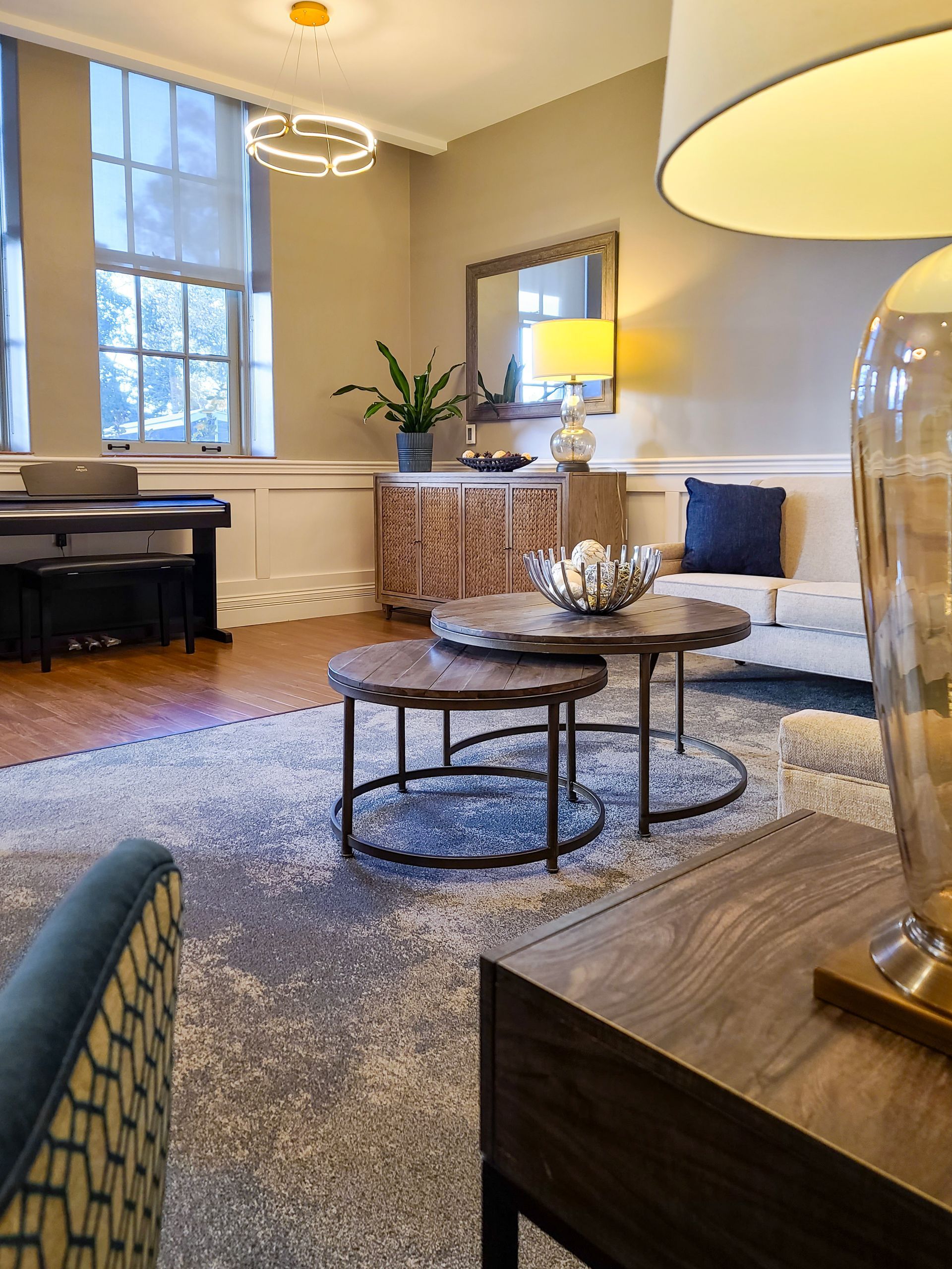 Elegant living room with piano, fireplace, large windows, and round coffee table on a textured rug