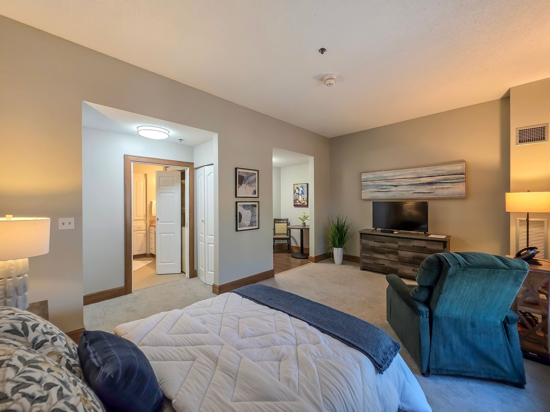 A bedroom featuring a bedside table, a stacked washer and dryer unit in a small closet, and an adjacent bathroom door.