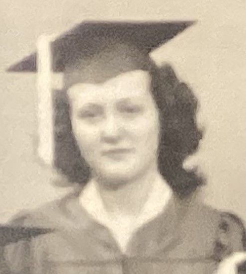 A sepia-toned headshot of a person wearing a graduation cap and gown, looking directly at the camera.