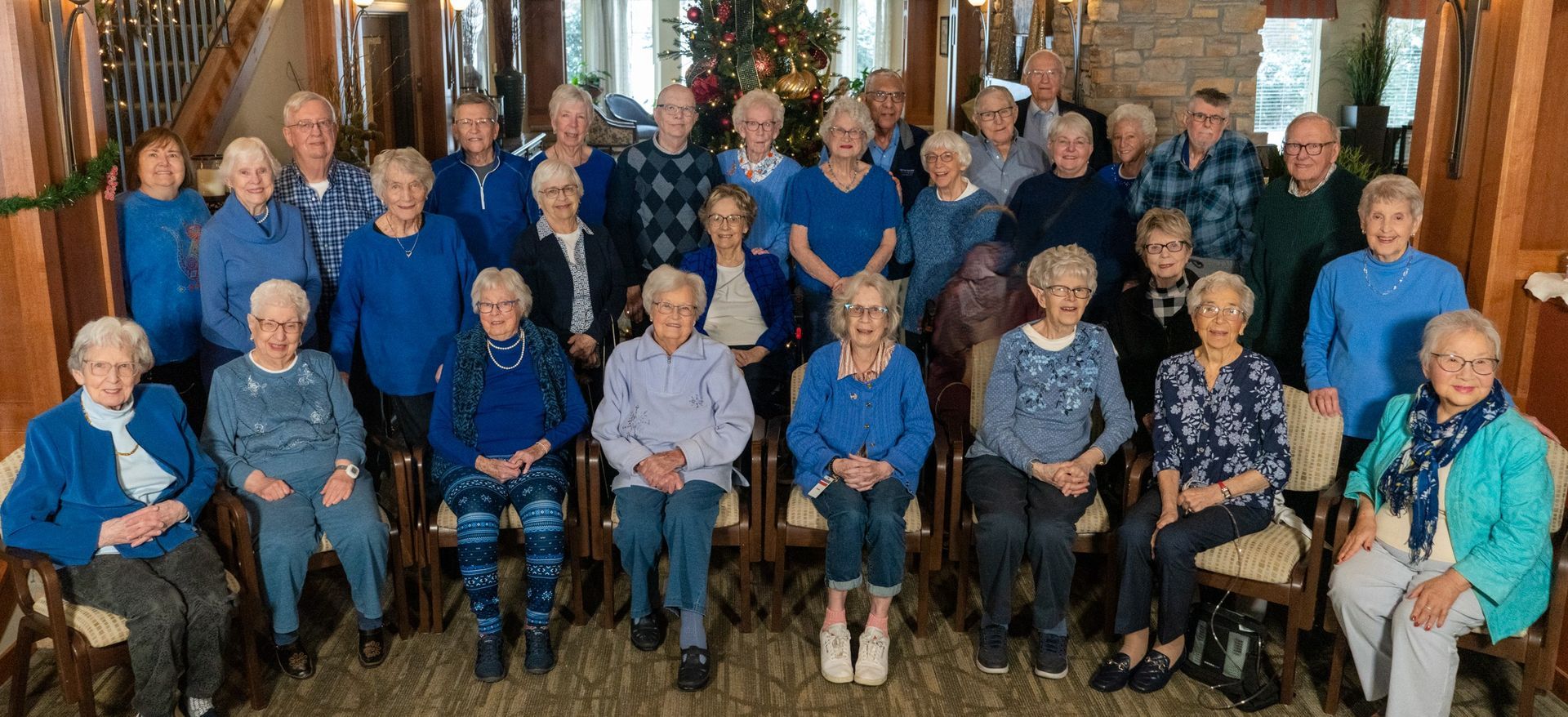 Group of people posing indoors in front of a staircase, many wearing blue clothing.