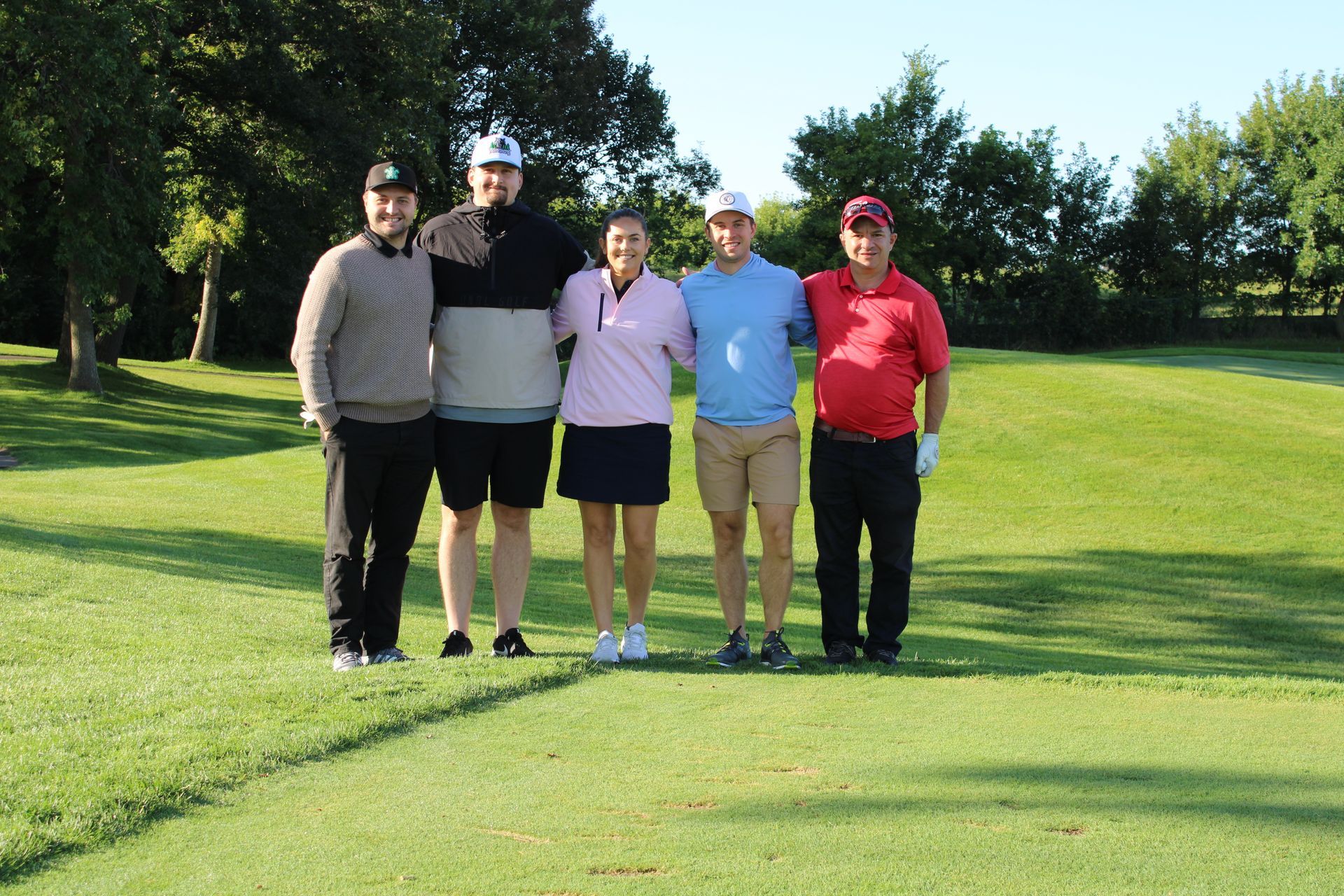 Five people stand in a line on a sunny golf course, smiling for a group photo.