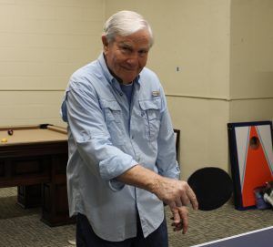 A person in a light blue button-down shirt holding a table tennis paddle, standing in a room with game tables.