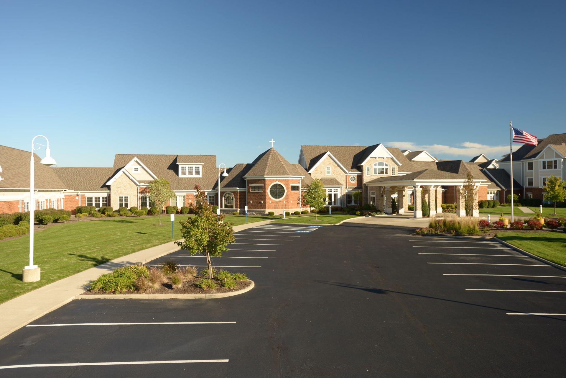 A multi-story beige building with a gray roof and a paved parking lot in the foreground under a clear blue sky.