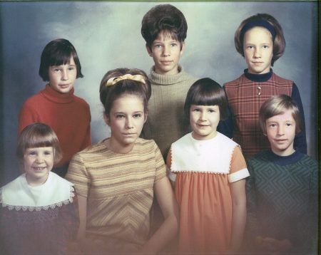 A vintage portrait of seven people posed in front of a mottled grey backdrop, wearing coordinated late-1960s style clothing.