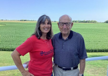 A person in a red shirt and a person in a navy blue polo shirt stand side-by-side in front of a green field.