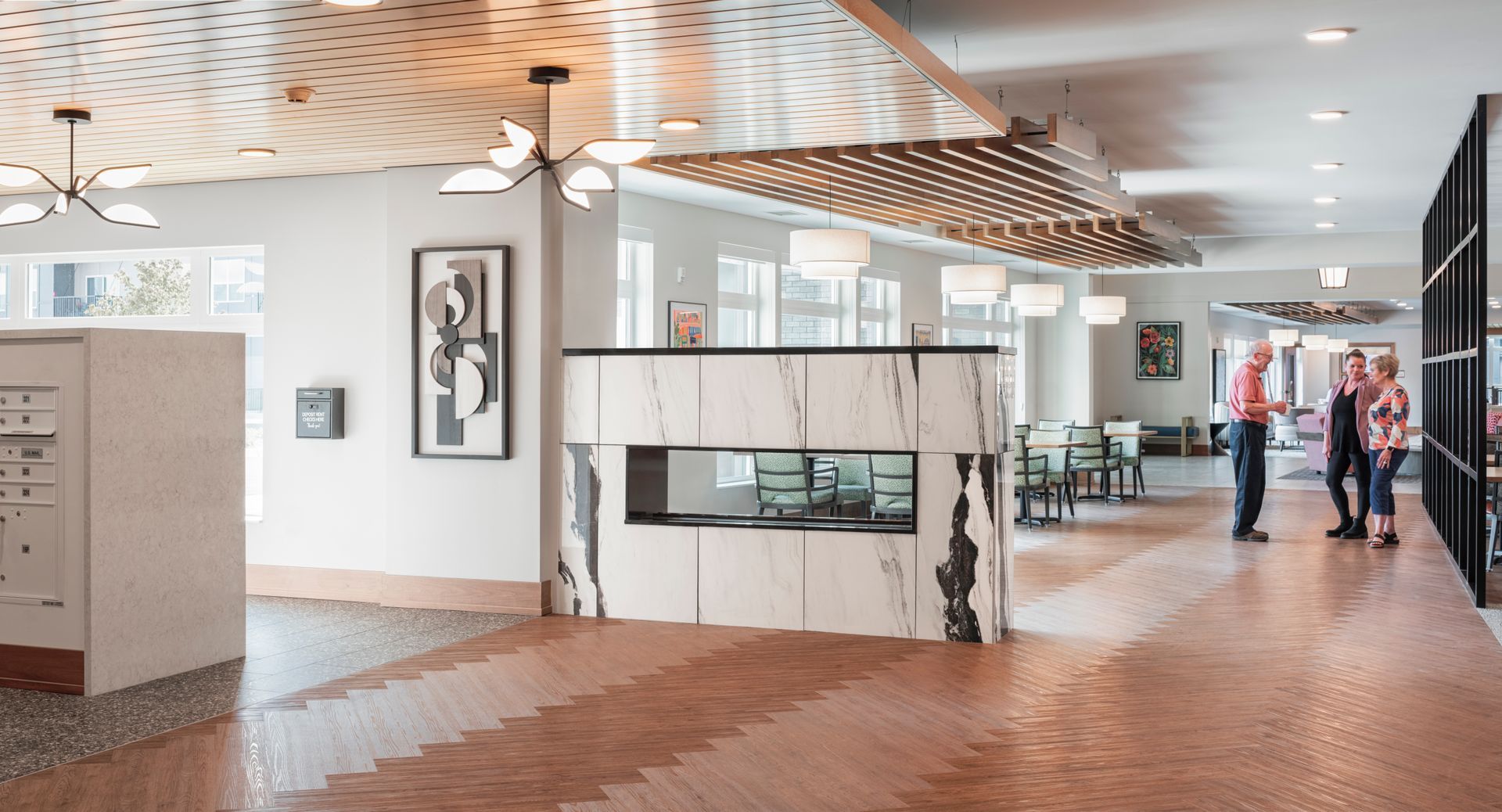 Modern interior lobby with a patterned ceiling, marble-faced fireplace, and people standing in a bright, open space.