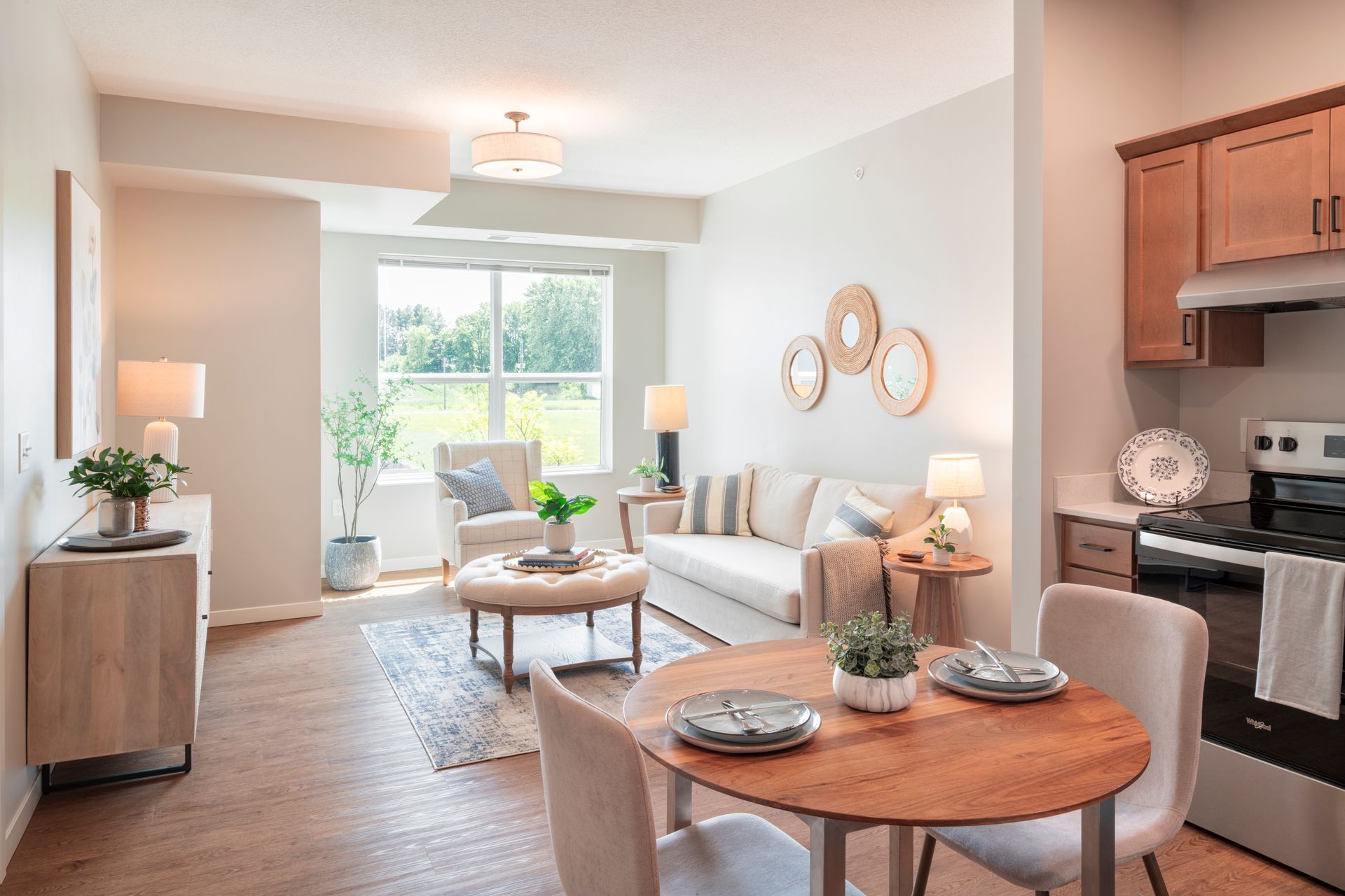 A bright, open-concept living area featuring a kitchen, dining table, and sofa with soft, neutral decor and wood accents.