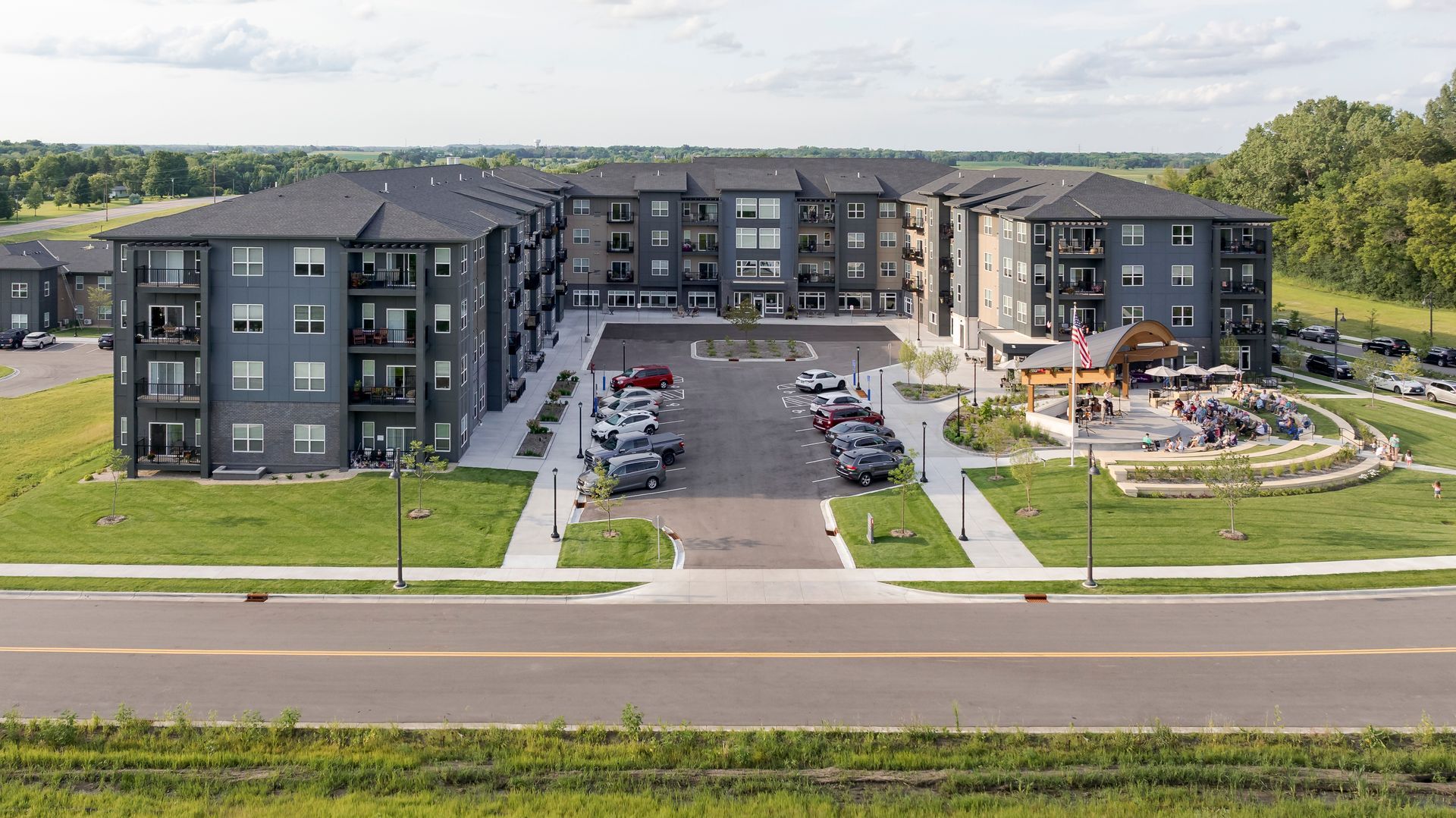 An aerial view of a dark gray, multi-story apartment complex with a central parking lot and an outdoor patio area.