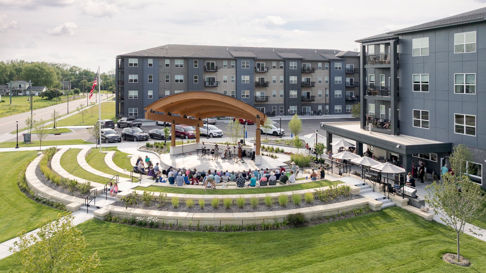 An outdoor amphitheater with a curved stage and tiered seating, filled with people watching a performance near apartments.