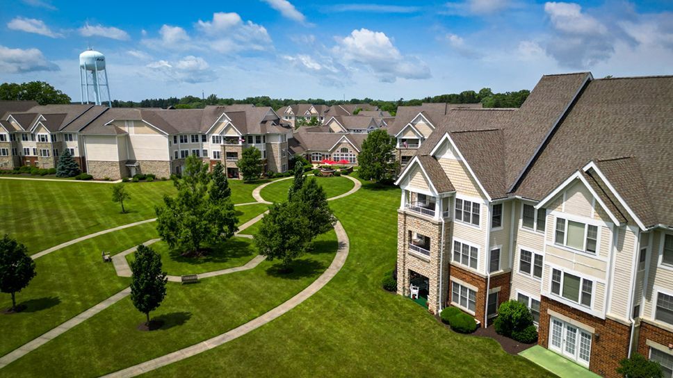 Aerial view of multi-story apartment buildings with tan siding and brick, surrounded by green lawns and walkways.
