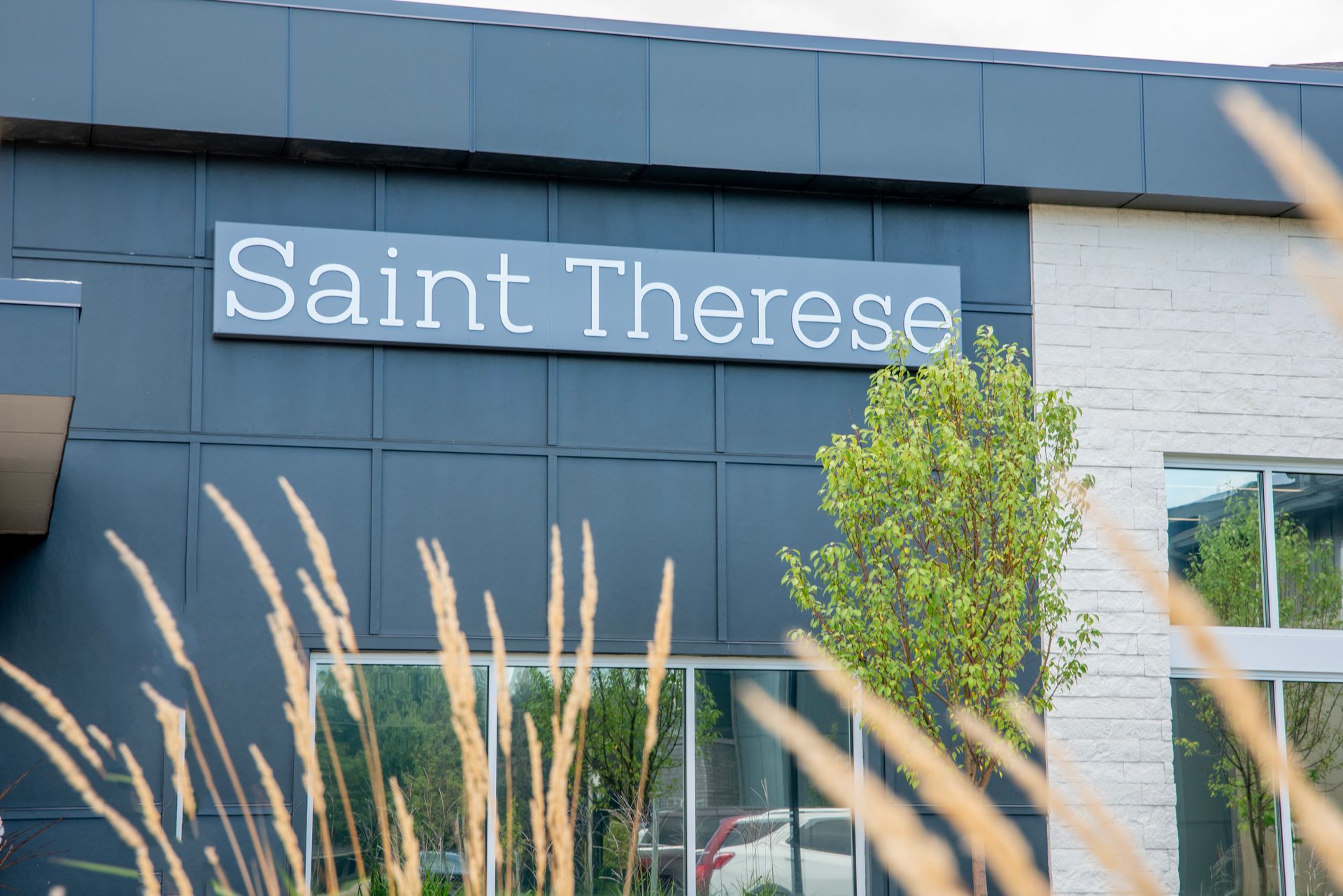 The exterior of a Saint Therese building, featuring a dark blue facade with white lettering and a light stone wall.