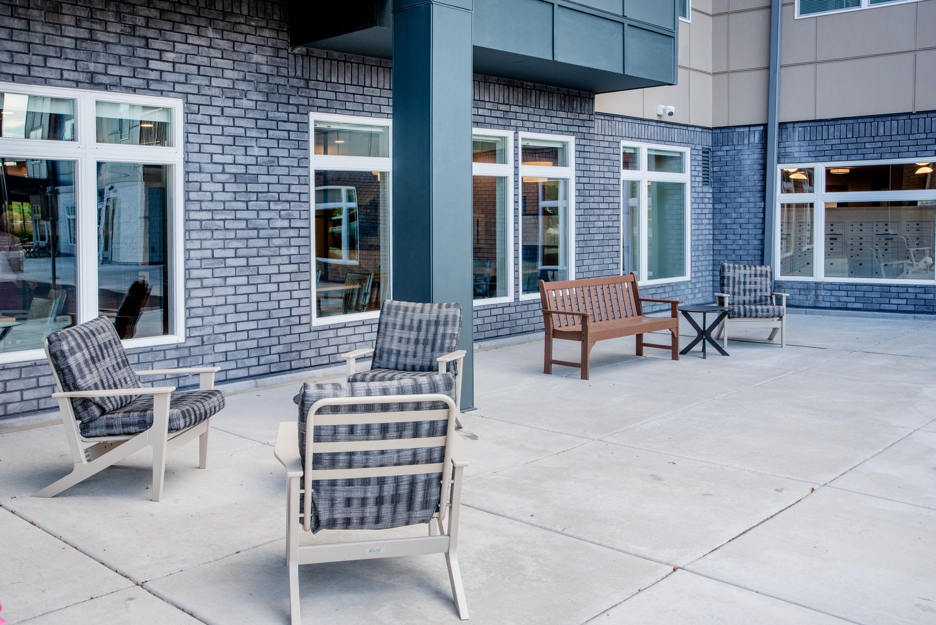 A patio with grey brick walls, featuring a wooden bench and several chairs arranged on a paved outdoor area.
