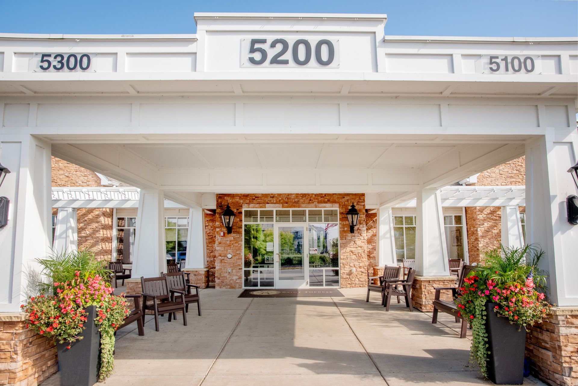 A white-covered entrance to a building labeled 5200, featuring stone walls, potted flowers, and outdoor patio furniture.