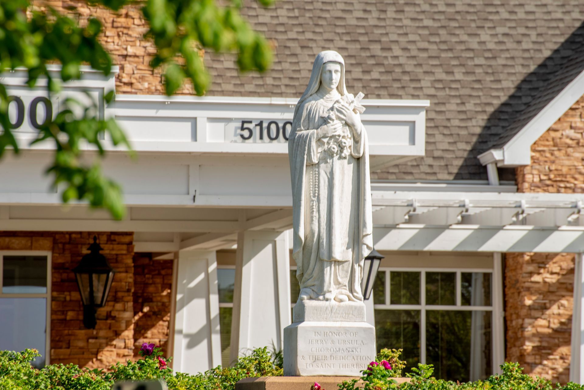 A white stone statue of a figure holding a cross, standing in front of a building with the number 5100 on its facade.