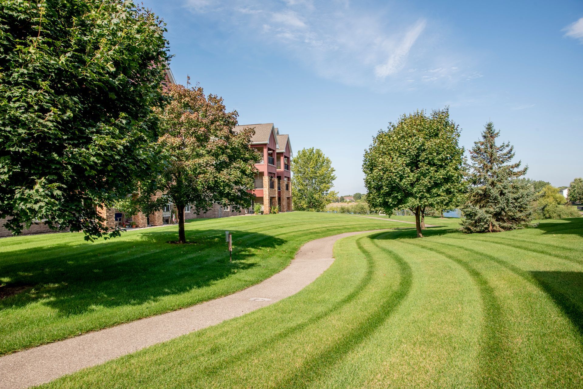 A gravel path winds through a bright green lawn toward a brick building under a clear blue sky.