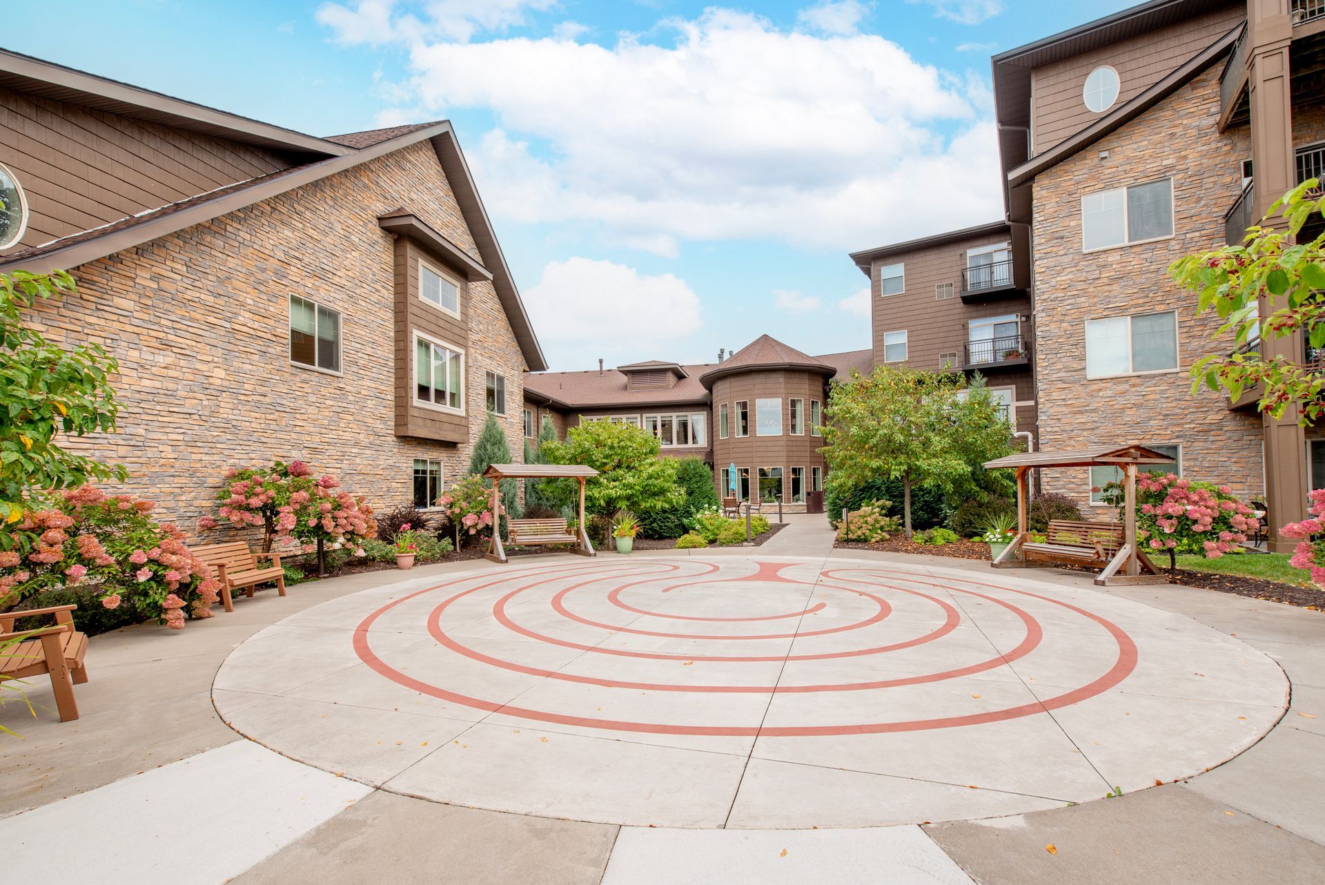 Apartment courtyard with circular red pattern paving, brick buildings, and flowers under a blue sky