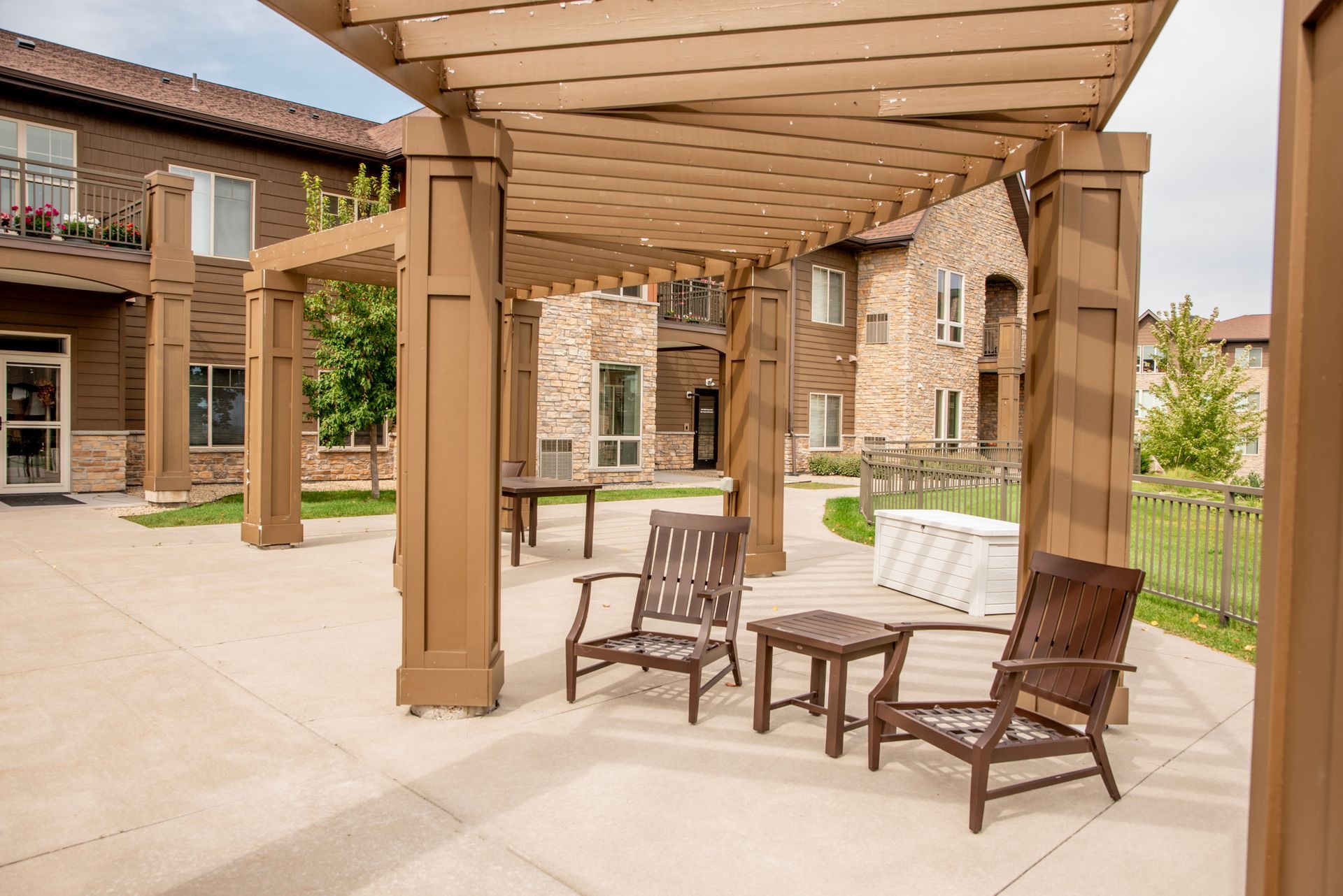 Covered patio with wooden pergola, wicker seating, and stone courtyard in a rustic building complex