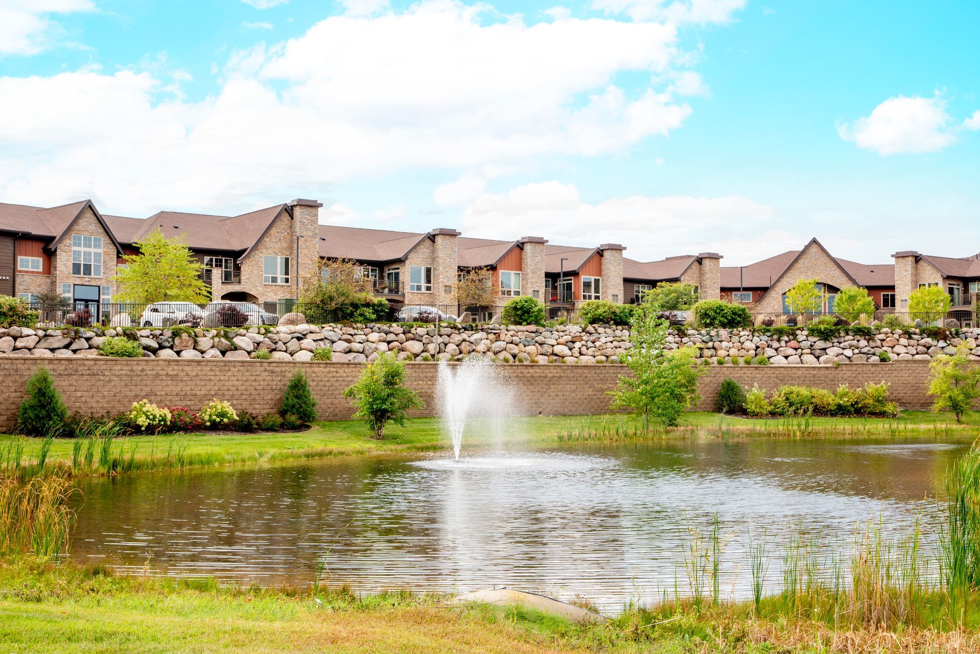 Suburban homes beside a pond with a fountain under a bright blue sky