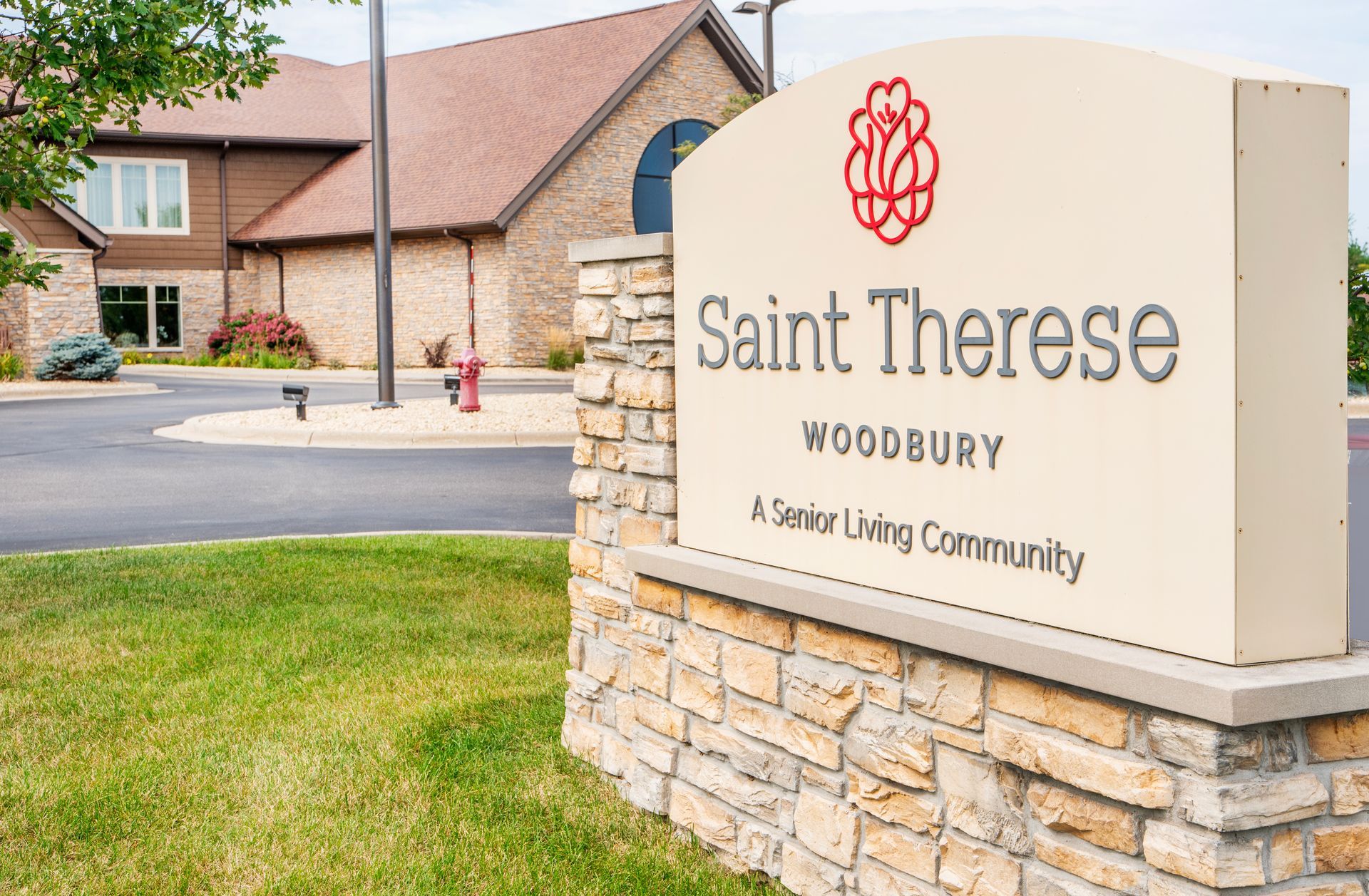 Saint Therese Woodbury community entrance sign beside a brick building and landscaped lawn