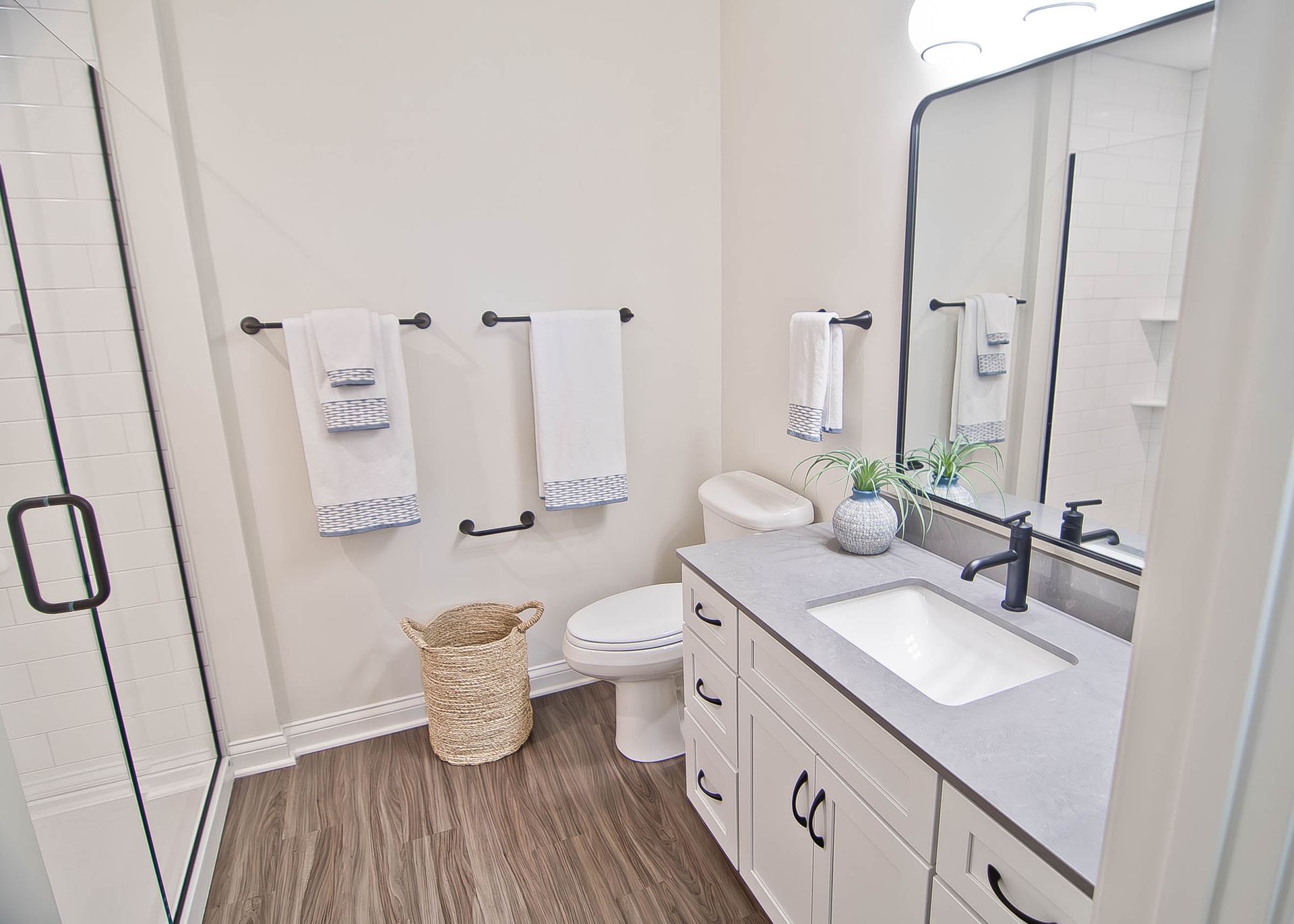 A modern bathroom with a white vanity, grey countertop, black fixtures, a glass shower, and a wicker basket on the floor.