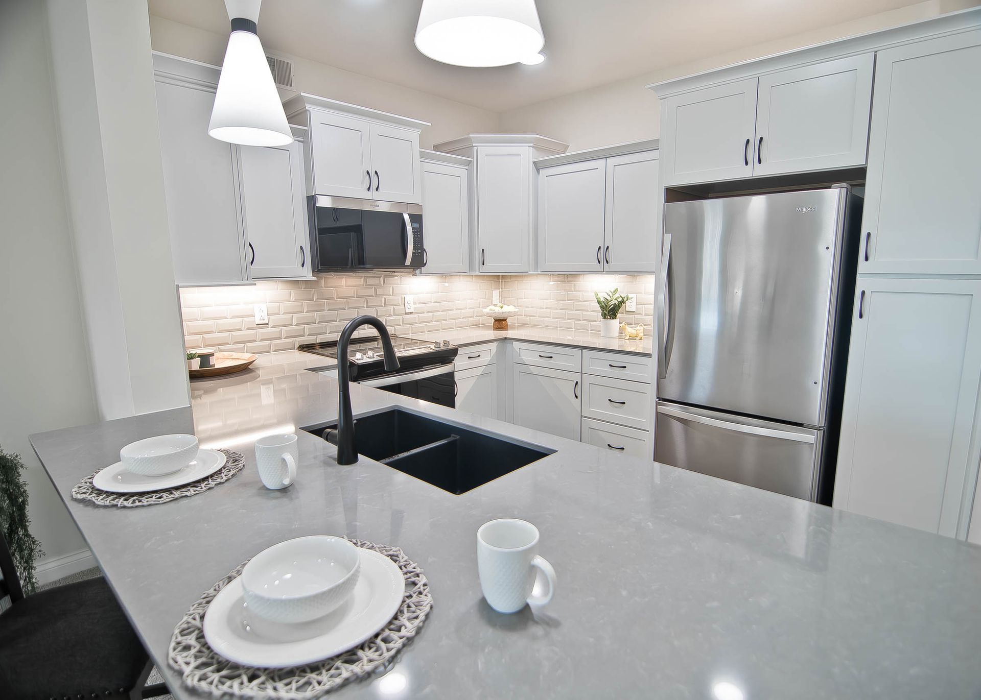 A modern kitchen featuring white cabinets, stainless steel appliances, and a gray countertop island set for dining.
