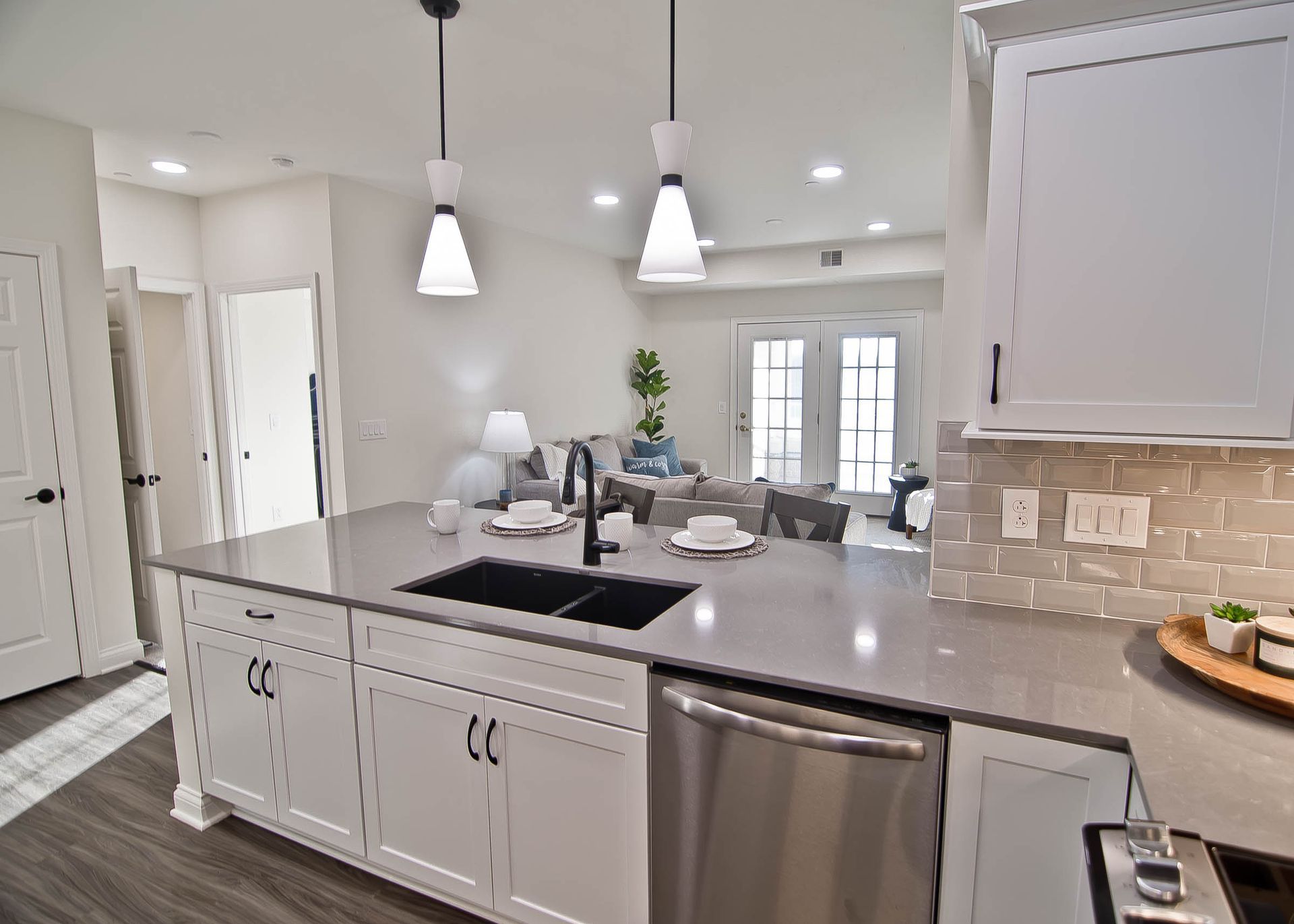 Modern kitchen island with gray quartz countertops and white cabinets, looking out toward a bright, open living room.