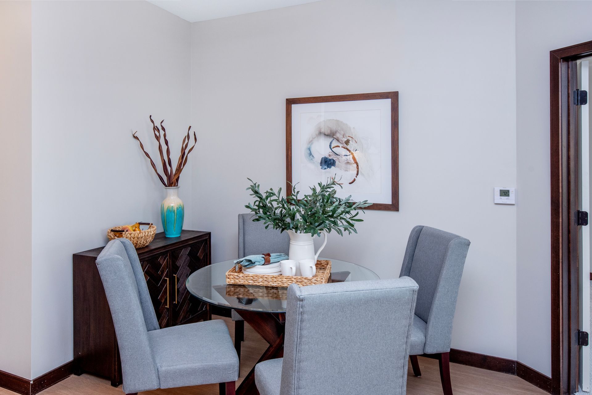 Small dining nook with four gray chairs, a round table, and a vase of flowers against white walls.