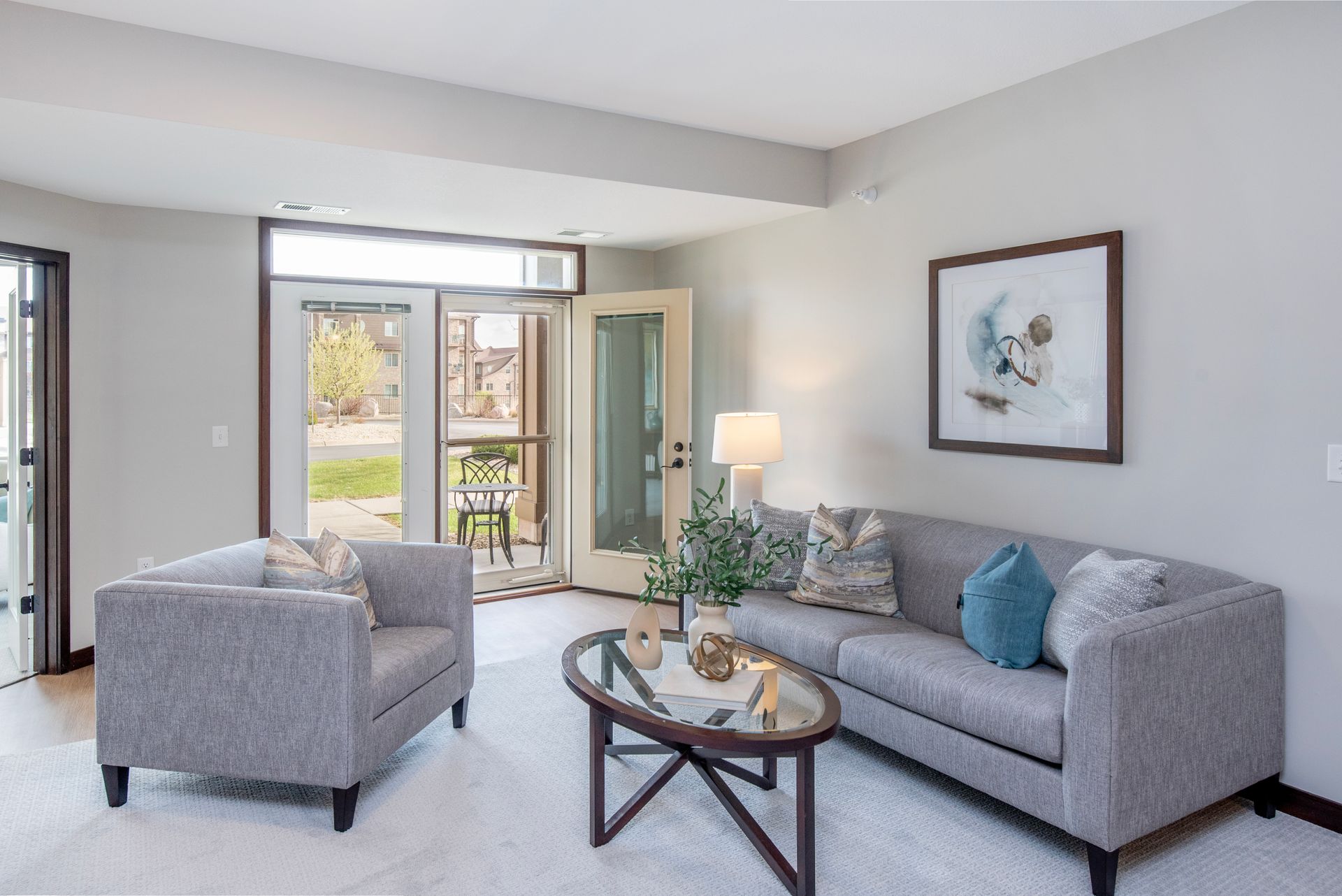 Bright living room with gray sofa, armchair, coffee table, lamp, and balcony doors.