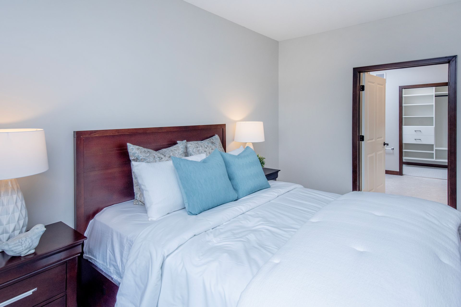 Bright bedroom with a bed, nightstands, lamps, and an open doorway to a bathroom in the background