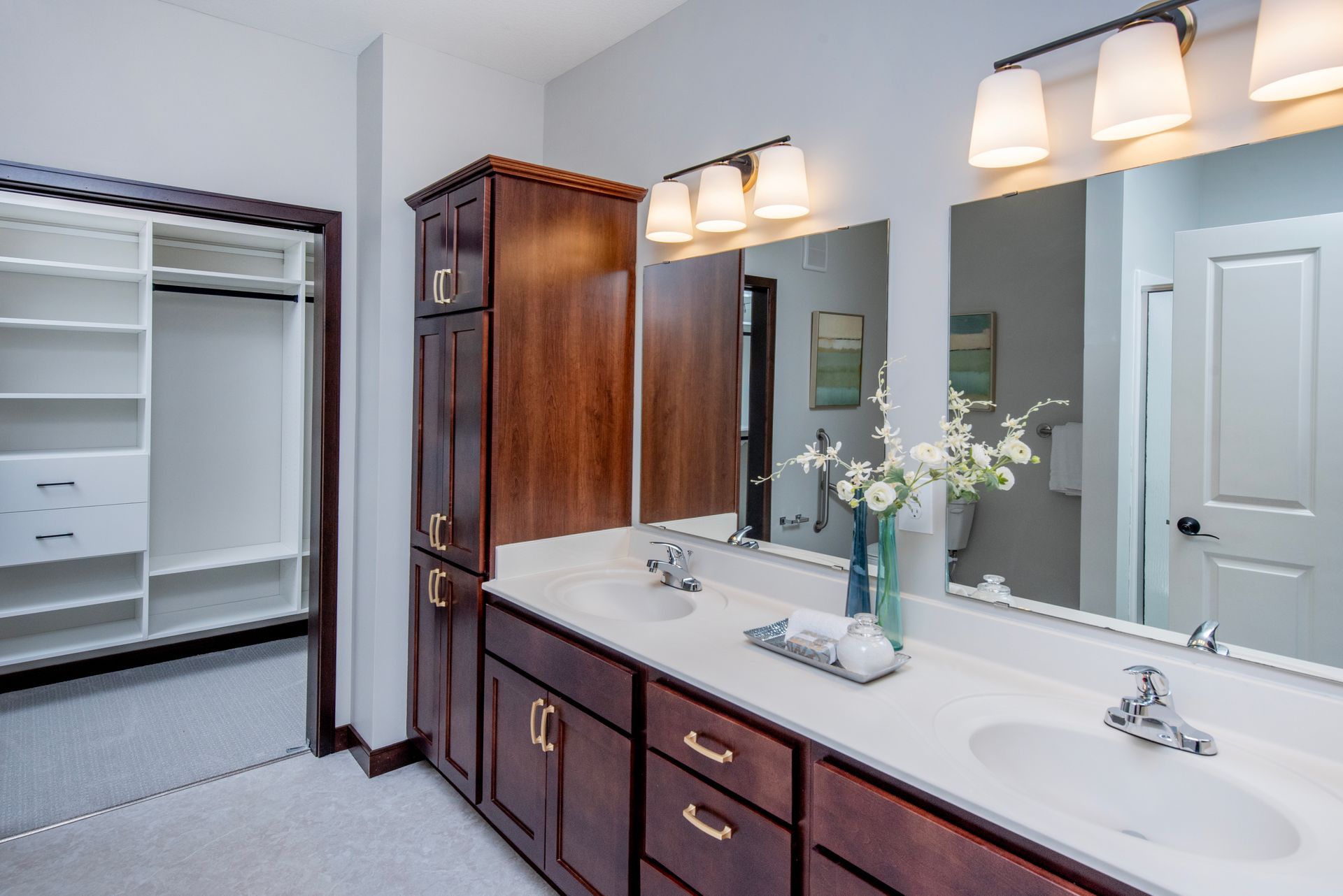 Bathroom vanity with double sinks, large mirror, dark wood cabinets, and open walk-in closet nearby