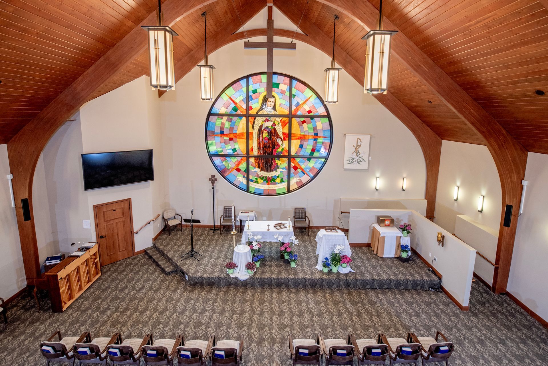 Church sanctuary with wooden ceiling, stained-glass window, altar, and rows of chairs facing the front
