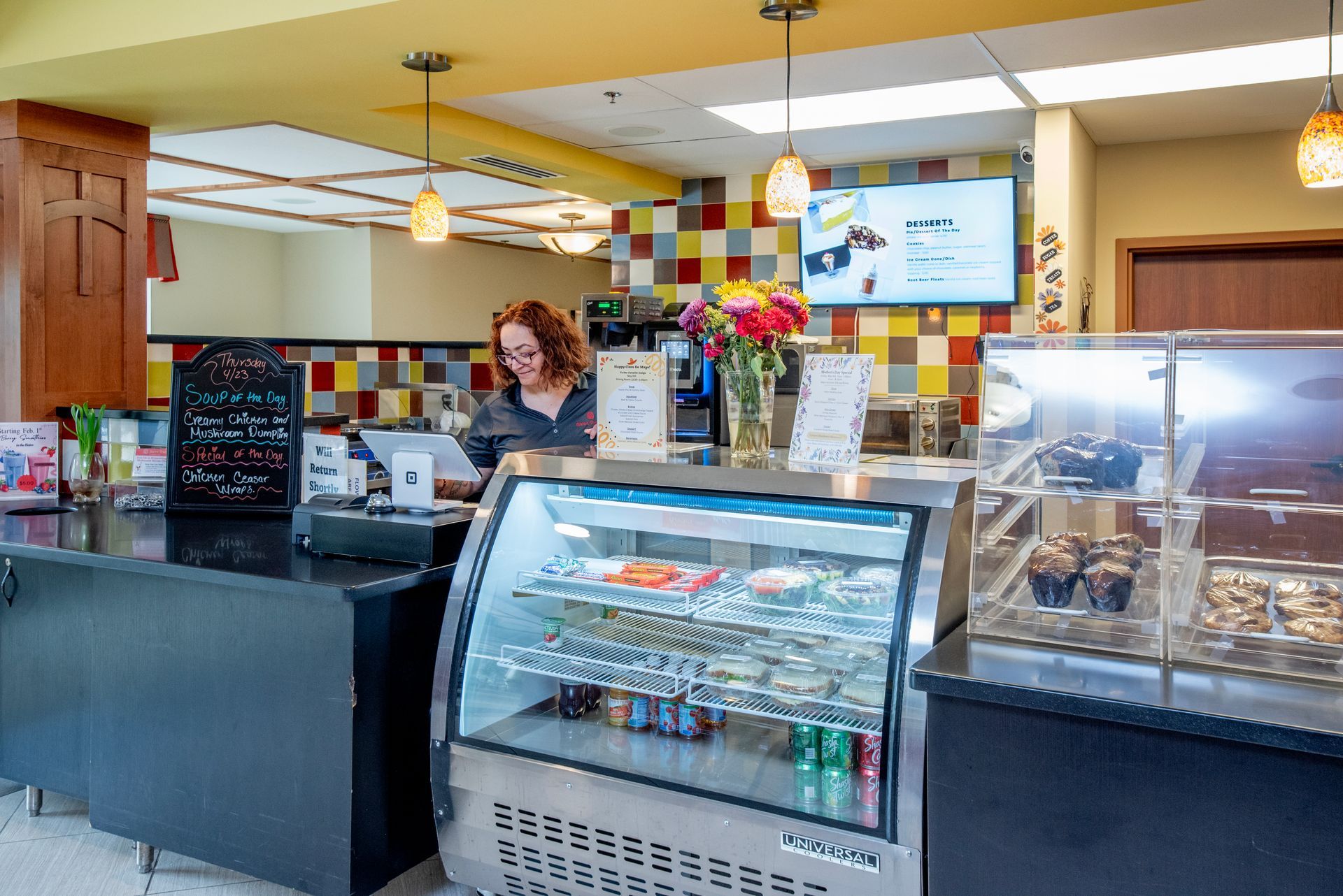 Ice cream shop counter with display case, menu board, and staff behind the register