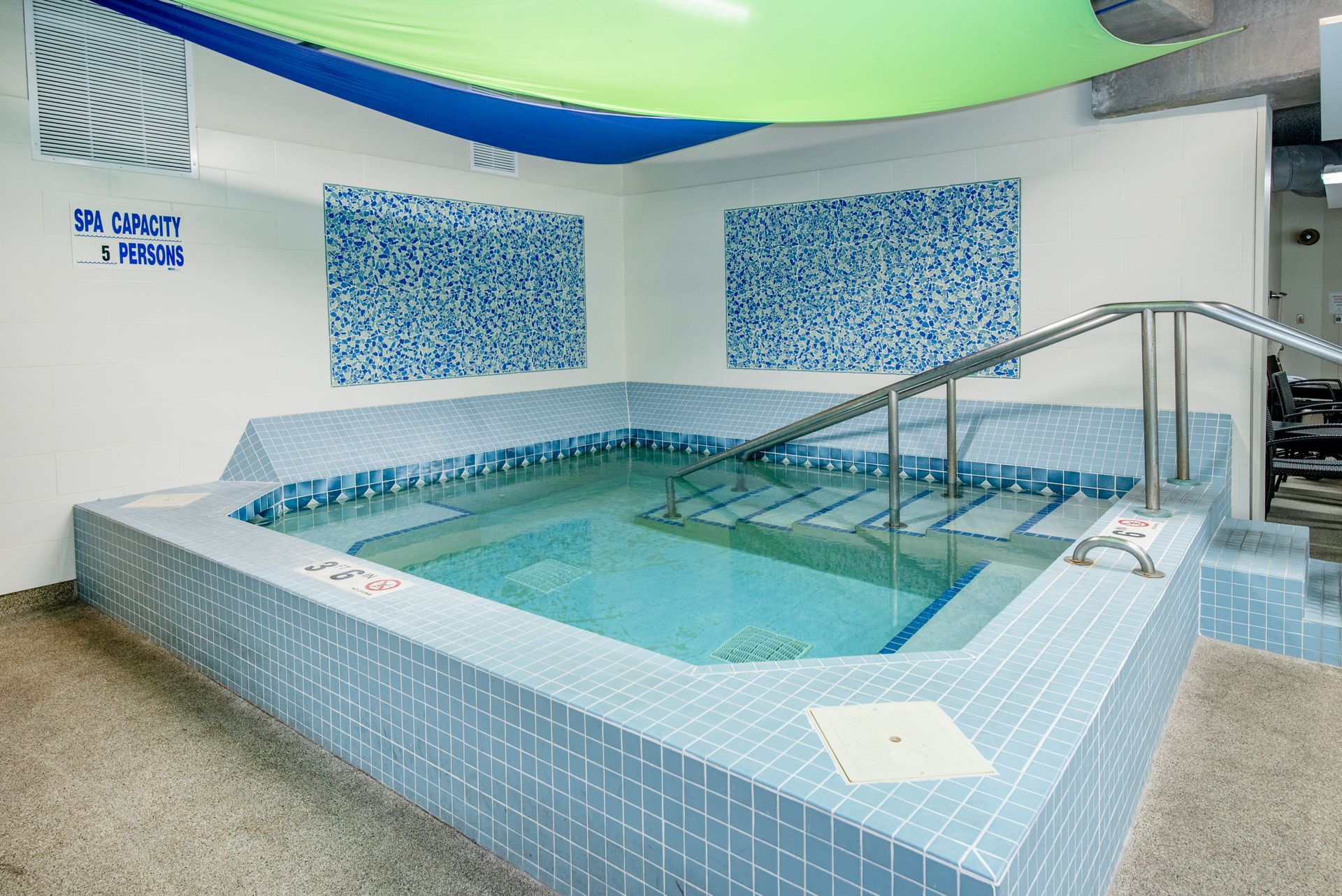 Indoor spa pool with blue tiled walls, handrails, and calm turquoise water