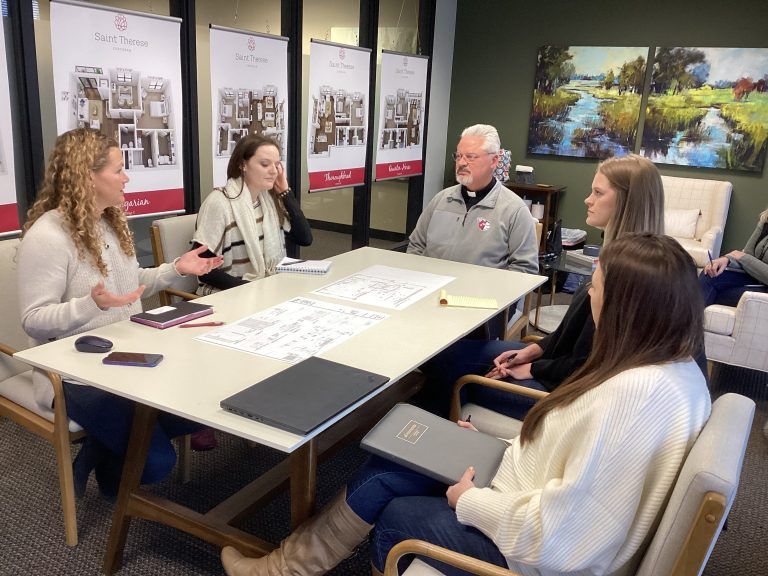 Four people sit around a table in an office, reviewing documents and discussing plans in front of display banners.
