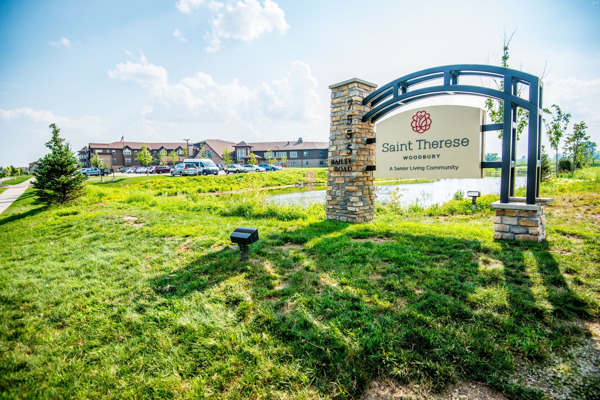 A stone monument sign for Cedar Meadows Senior Living Community stands in a green grassy field on a sunny day.