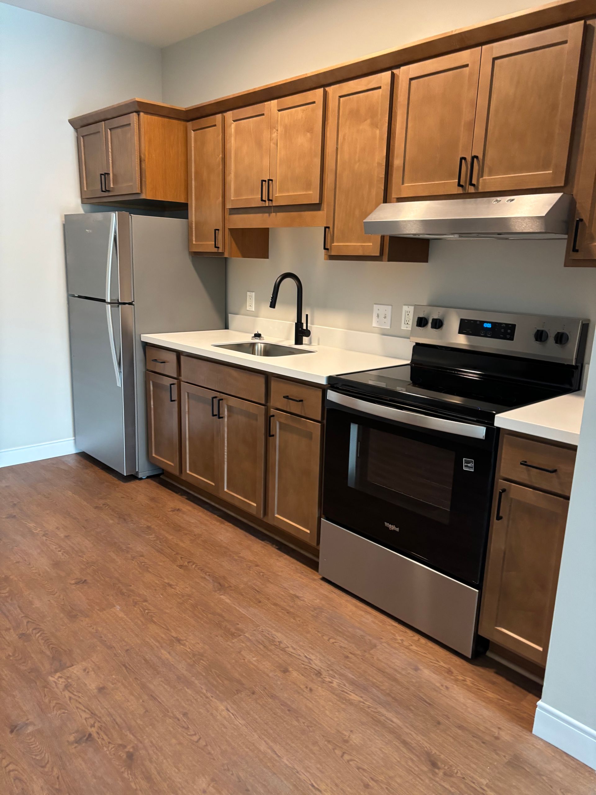Kitchen with wooden cabinets, stainless steel appliances, a black stove, and light countertops on wood-look flooring.