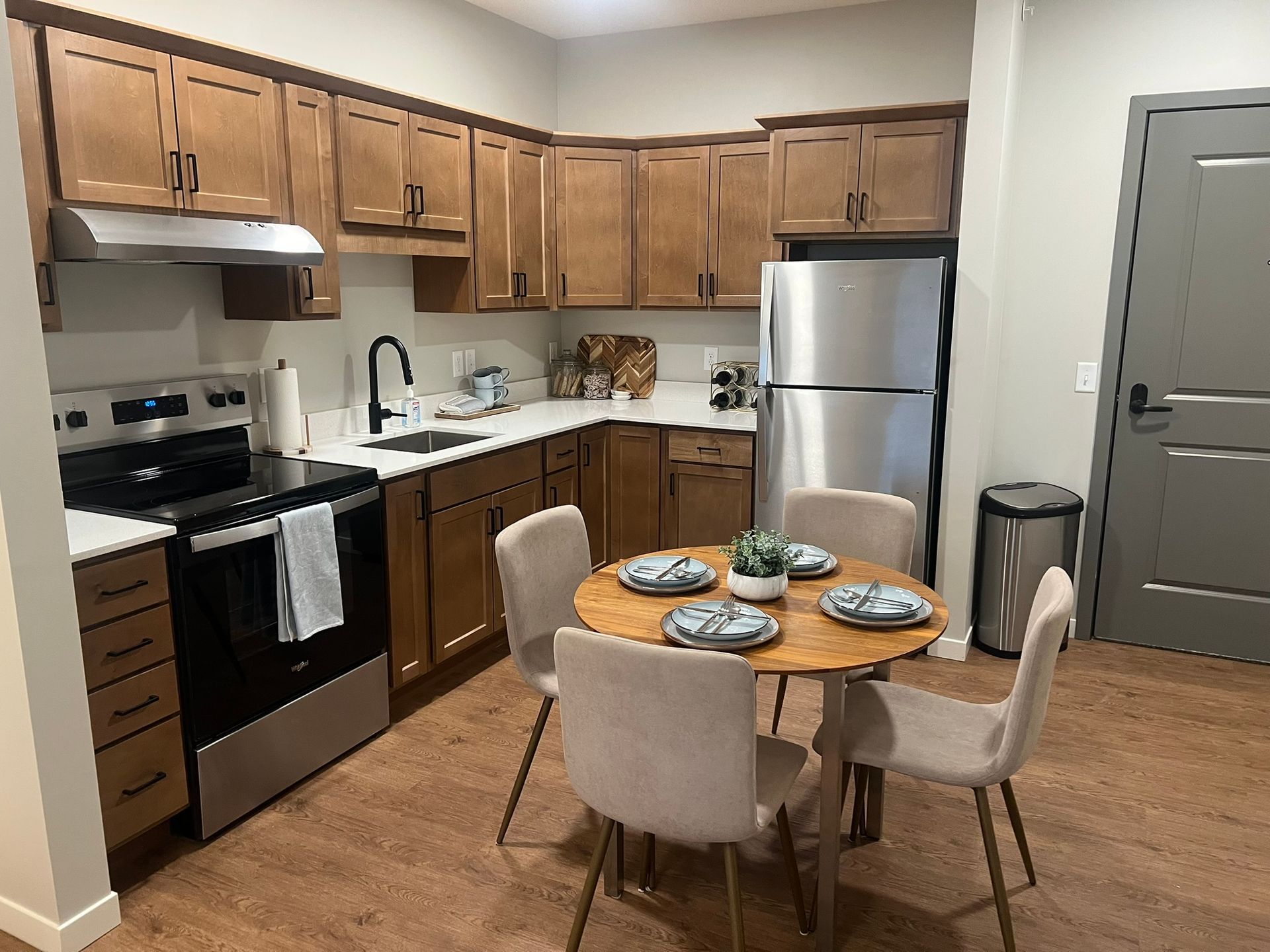 A kitchen with wood cabinets, stainless steel appliances, and a round dining table with four beige chairs.
