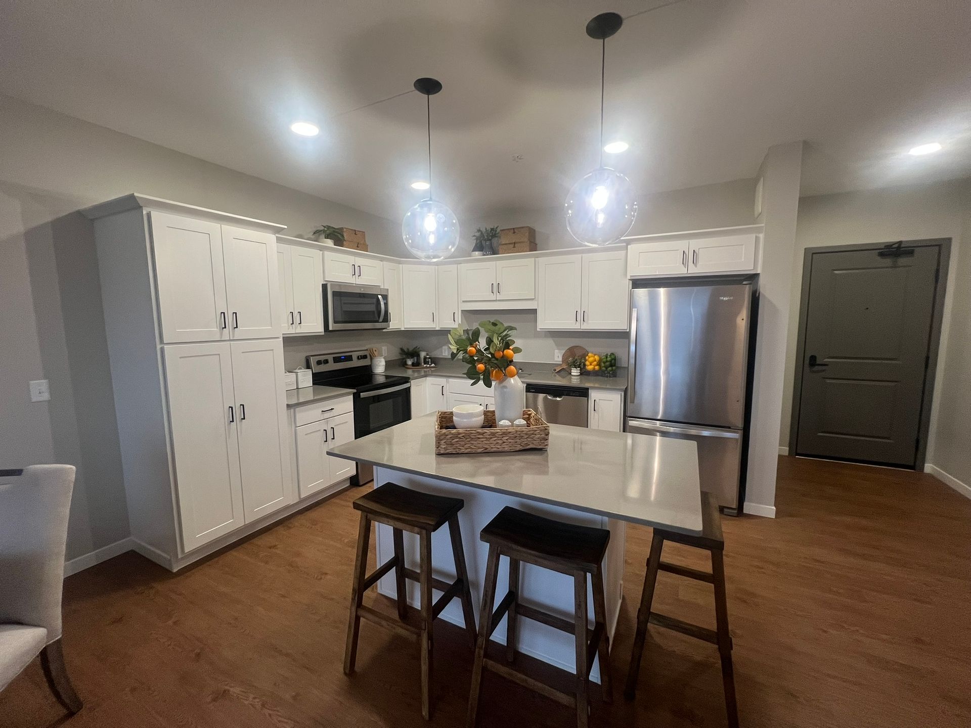 A modern kitchen featuring white cabinets, stainless steel appliances, a kitchen island with stools, and wood flooring.