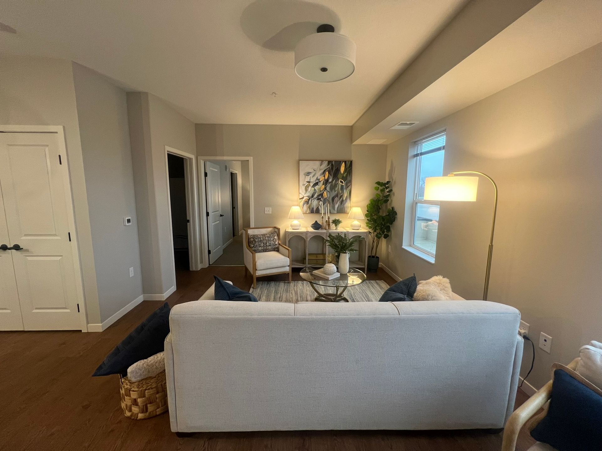 A modern living room with a light gray sofa facing a small console table, artwork, and an armchair under warm lighting.