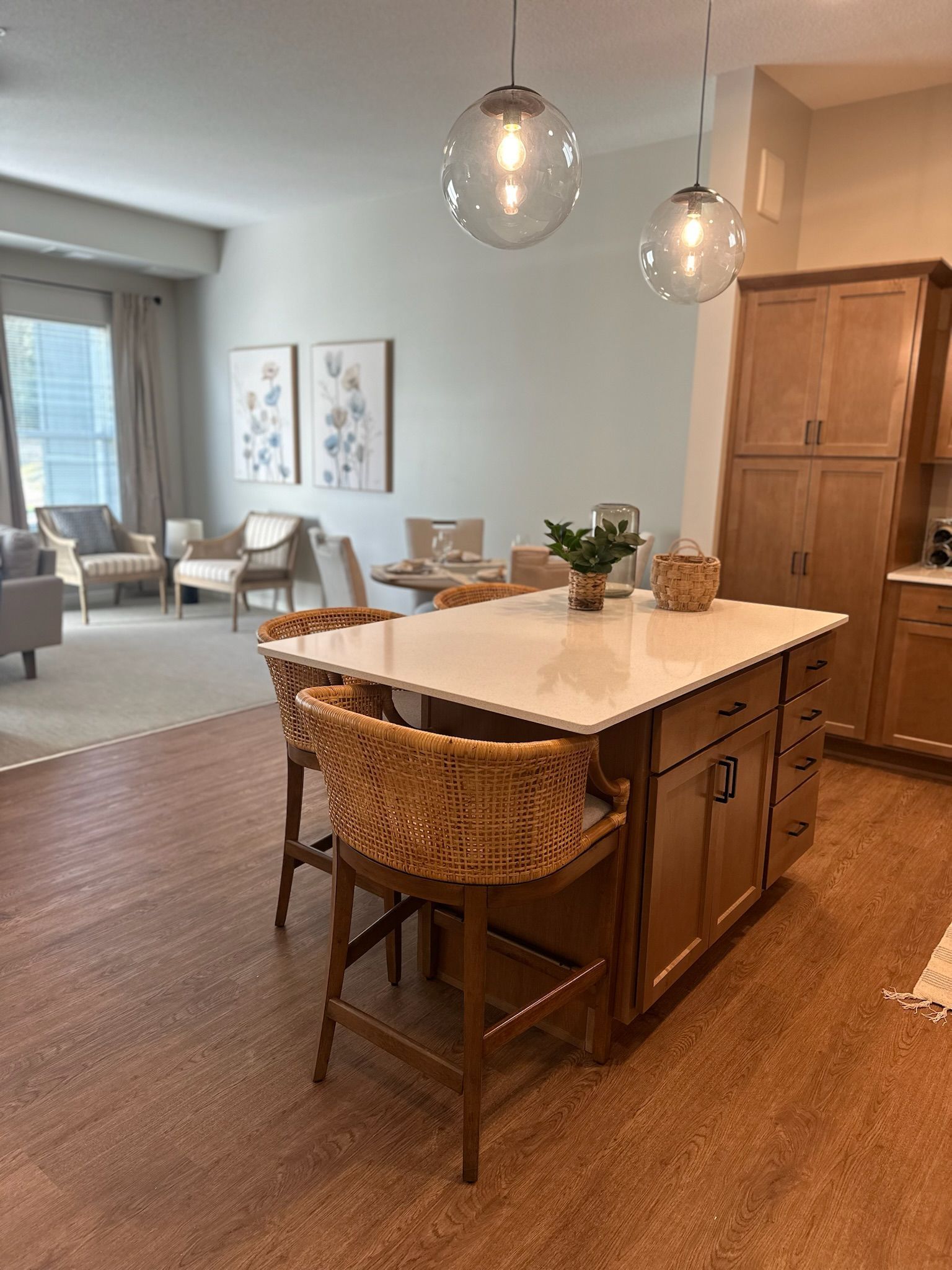 A kitchen island with two woven bar stools, two globe pendant lights, and a living area visible in the background.