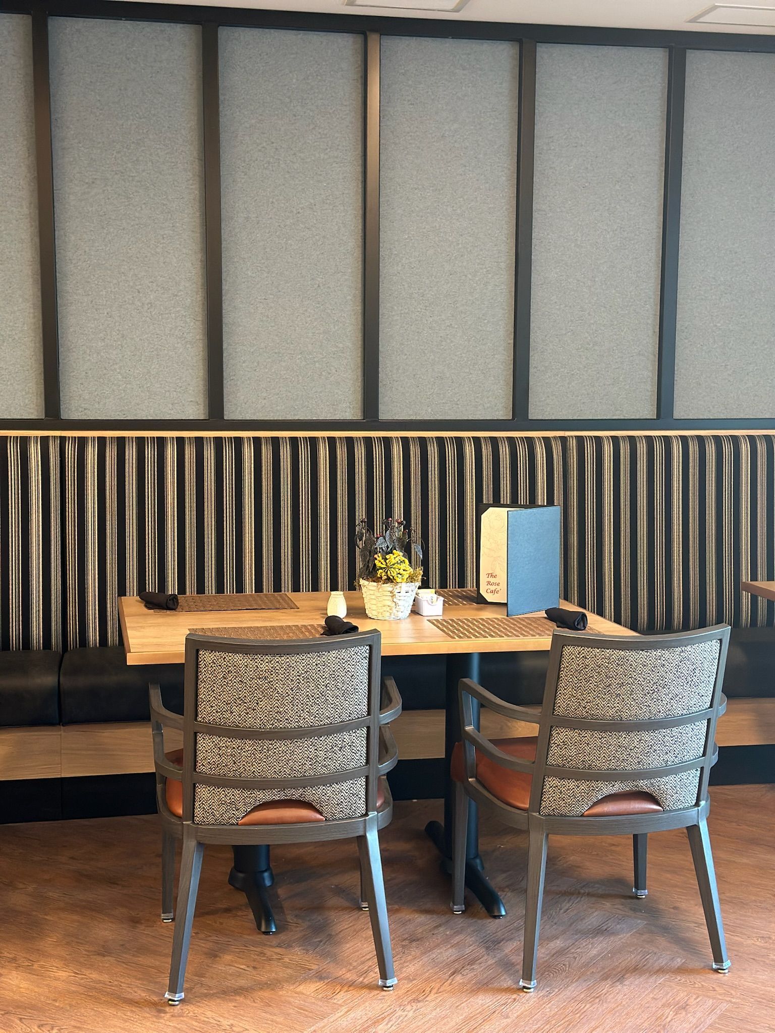 A restaurant dining area featuring a wooden table with two chairs, set against a wall with textured panels and drapery.