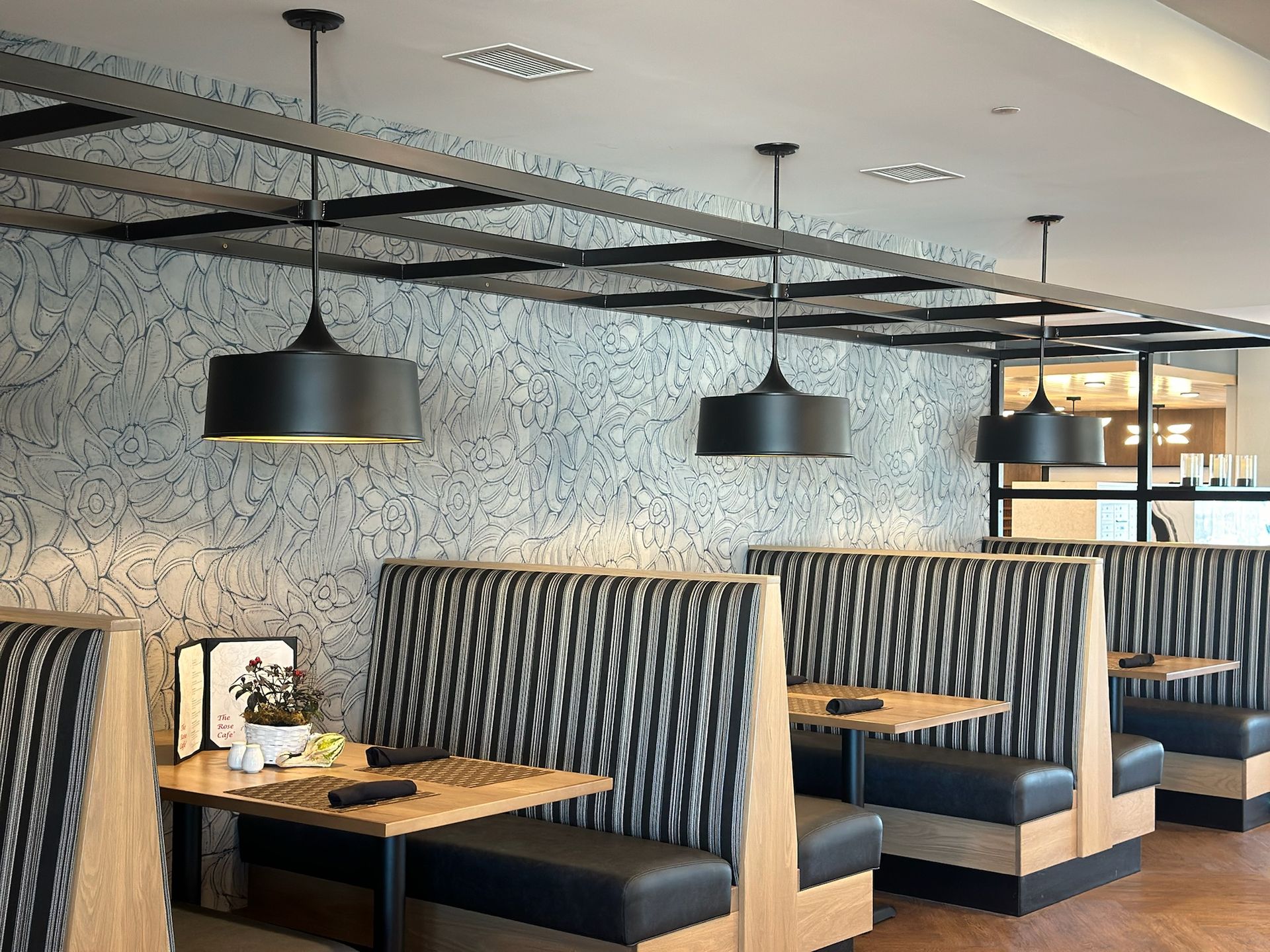 Modern restaurant interior with wooden booths, patterned fabric seating, and hanging pendant lights against a mural wall.